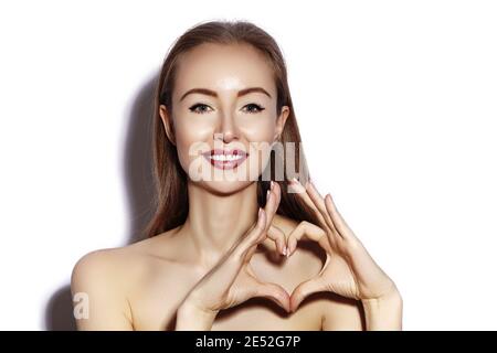 Romantische junge Frau macht Herz-Form mit ihren Fingern. Liebe und Valentinstag Symbol. Mode Mädchen mit Happy Smile auf weißem Hintergrund. Stockfoto