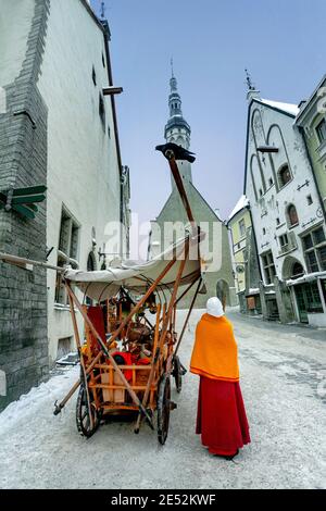 Blick auf den Rathausturm. Straßenszene mit Verkäufer in mittelalterlicher traditioneller Kleidung in der Nähe von antiken Holzwagen in der Altstadt am Wintertag. Tallinn, Estoni Stockfoto