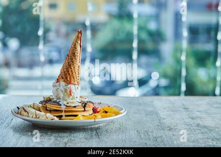 Pfannkuchen mit Eiskegel, Mandarine, Erdbeere, Banane und Schokoladensirup in der weißen Platte auf dem Marmorboden Stockfoto