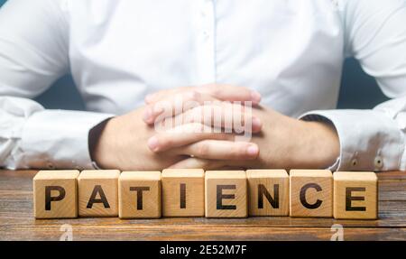 Der Mensch faltete seine Hände auf einem Hintergrund von Blöcken mit dem Wort Geduld. Geduld in Erwartung, Ausdauer. Widerstand gegen Stress, Ruhe. Clar Stockfoto