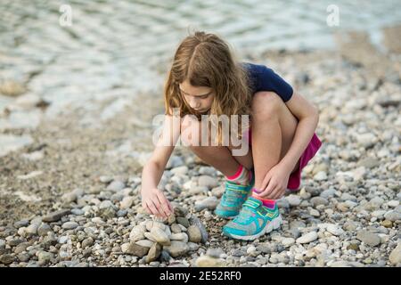 Ein elfjähriges Mädchen stapelt am Ufer der Isar in München Steine in eine Kaira. Stockfoto