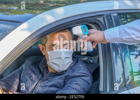 Die Sicherheit misst die Körpertemperatur des Fahrers mithilfe eines digitalen Infrarot-Thermometers. Temperaturinspektion inmitten einer Coronavirus-Pandemie (covid-19). Stockfoto