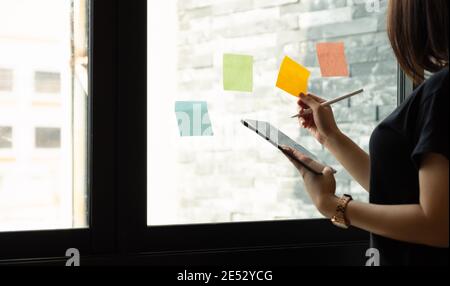 Geschäftsfrau mit Tablet während Post IT Notizen Idee diskutieren und planen in Glaswand im Tagungsraum, Geschäftskonzept. Stockfoto