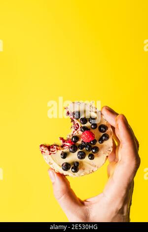 Hand halten knusprig aufgeblasen Reiskuchen mit frischen Früchten Blaubeeren Himbeeren vor dem gelben Hintergrund - gesund Bio-Vegetarier oder ve Stockfoto