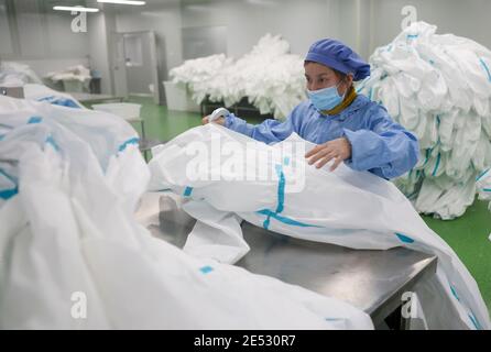 Chongqing, China. Januar 2021. Ein Arbeiter inspiziert die Qualität von Schutzanzügen in einer Werkstatt im Landkreis Fengdu in Chongqing, Südwestchina, 25. Januar 2021. Die Fabrik produziert rund um die Uhr Schutzanzüge, um die Binnennachfrage zu befriedigen, während das Land gegen den jüngsten Ausbruch der COVID-19-Fälle kämpft. Quelle: Liu Chan/Xinhua/Alamy Live News Stockfoto