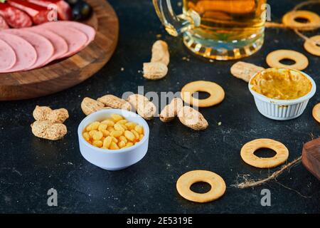 Ein Teller Würstchen, verschiedene Snacks und ein Glas Bier auf einem dunklen Tisch Stockfoto