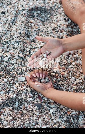 Die Hände eines omans spielen mit Muscheln am Strand Stockfoto