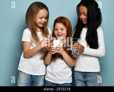 Drei fröhliche Kinder Mädchen Freunde in weißen T-Shirts teilen ihre Lieblings-Getränke Wasser, Milch und Saft Toasting feiern Stockfoto