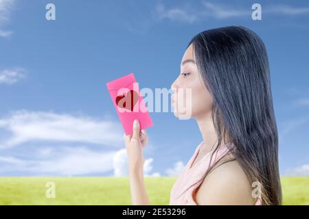 Asiatische Frau hält einen rosa Umschlag mit Herz mit einem blauen Himmel Hintergrund. Valentinstag Stockfoto