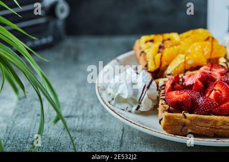 Waffeln mit Eis, Banane, Erdbeere, Schokolade auf der weißen Platte auf dem Marmorboden Stockfoto