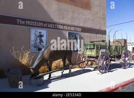 Vintage Western Wagon Wheel Replik vor dem Museum of Western Film History in Lone Pine, Kalifornien mit alten Filmplakaten an der Außenwand Stockfoto