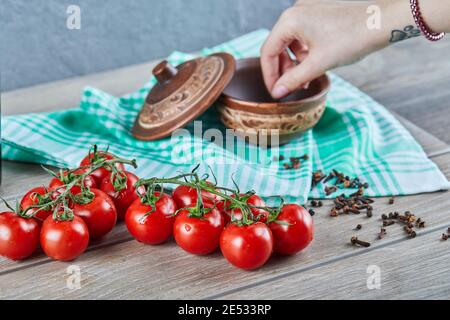 Tomaten mit Zweig und Frau Hand nehmen Nelken Aus einer Schüssel auf einem Holztisch Stockfoto