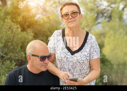 Porträt einer schönen älteren Frau und einem attraktiven Mann im Alter mit Handy in der Natur bei Sonnenuntergang. Stockfoto
