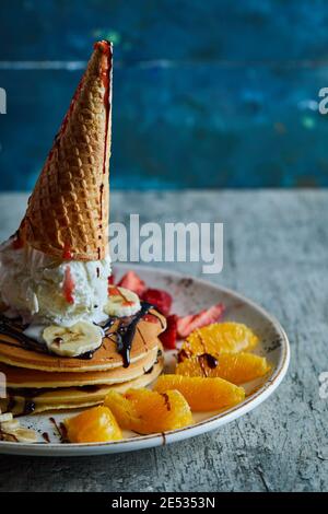 Pfannkuchen mit Eiskegel, Mandarine, Erdbeere, Banane und Schokoladensirup in der weißen Platte auf dem Marmorboden Stockfoto