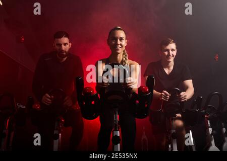 Fit Menschen Reiten Ergometer im Fitnessstudio, genießen Trainingszeit, in rauchigen roten Neon-Raum Stockfoto