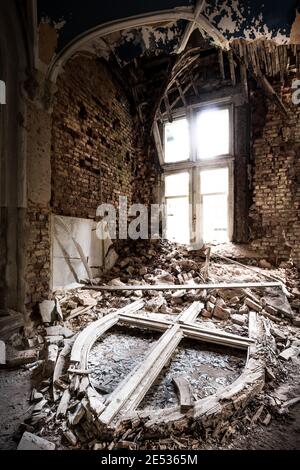 Das Innere eines alten verlassenen barocken Schlosses, mit einem spitzen Bogenfensterrahmen, der auf dem Boden unter Trümmern liegt Stockfoto