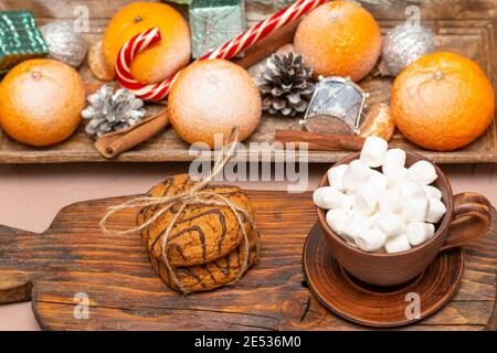 Haferflockenplätzchen und Kaffee mit Marshmallows auf einem Weihnachtstisch mit Zitrusfrüchten. Nahaufnahme, selektiver Fokus. Stockfoto