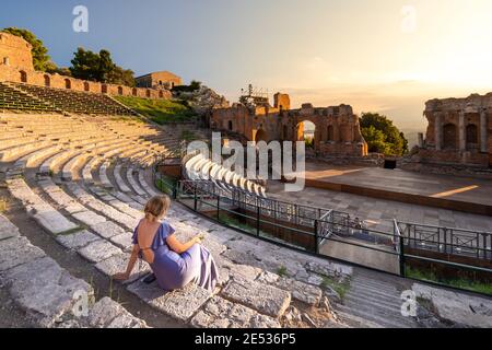 Eine in Purpur gekleidete Frau erschaut einen dramatischen Sonnenuntergang am Griechischen Theater in Taormina, Sizilien Stockfoto