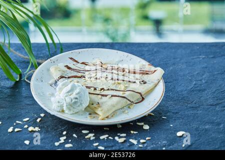 Pfannkuchen mit Eis, Streuseln, Schokolade auf dem weißen Teller im dunklen Hintergrund Stockfoto