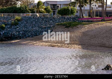 Ein kleiner Strand neben einer Hafenmauer und davor Des Wohnviertels am Meer in spätnachmittäglichen Schatten Stockfoto