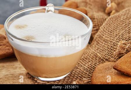 Eine Tasse Cappuccino-Kaffee und Lebkuchen in der Form eines Herzens auf einem Sackleinen Hintergrund Stockfoto