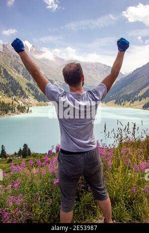 Ein Mann hob seine Hände zum Himmel neben einem Bergsee. Spektakuläre Landschaft auf Big Almaty See, Tien-Shan Berge in Almaty Region von Kasachstan. Vertikal Stockfoto