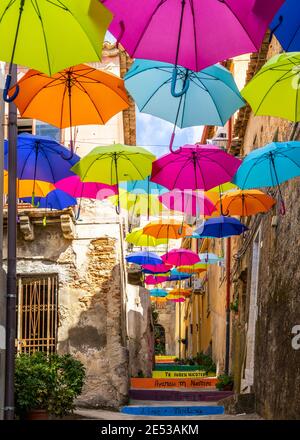 Typische schmale Straße mit bunten schwimmenden Sonnenschirmen in Nicotera, Kalabrien, Italien Stockfoto