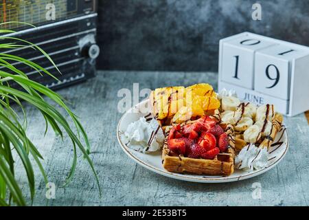 Waffeln mit Eis, Banane, Erdbeere, Schokolade auf der weißen Platte auf dem Marmorboden Stockfoto