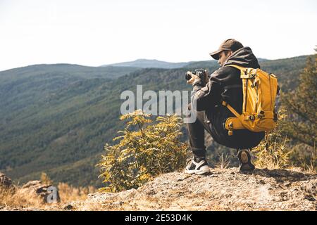 Ein Mann mit einem gelben Rucksack geht in der wandern Berge und macht Bilder von der Natur Stockfoto