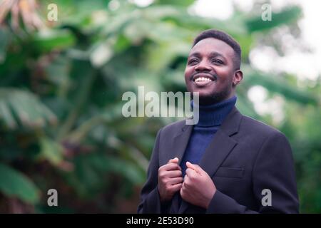 Schöner afrikanischer Geschäftsmann im trendigen formellen schwarzen Anzug. Kerl mit Bart trägt blaue Langarm oder Pullover Stockfoto