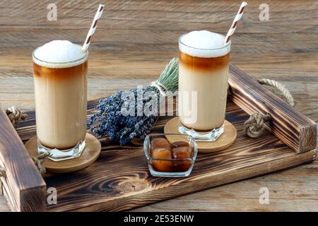 Kaffee Tasse Latte mit hausgemachtem Lavendelsirup und Blumen auf einem Holztablett. Gemütliches Frühstück Stockfoto