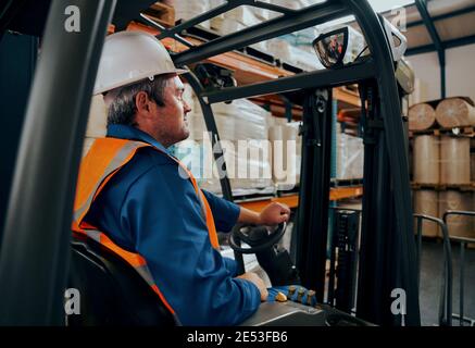 Seitenaufnahme eines männlichen Mitarbeiters, der den Gabelstapler fährt Im Lager Stockfoto
