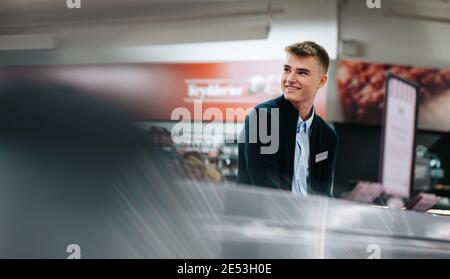 Junger männlicher Arbeiter, der in einem Supermarkt arbeitet. Mann auf einem Ferienjob im Lebensmittelgeschäft. Stockfoto