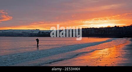 Portobello, Edinburgh, Schottland, Großbritannien. Januar 2021. Feuriger Sonnenaufgang für diesen Unterwasser-Kameramann und Filmmacher Mike Guest, am Ufer des Firth of Forth, mit den Hügeln von East Lothian im Hintergrund, die noch immer in einem kühlen Grad Celsius am Schnee festhalten. Stockfoto