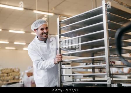 Junger Kaukasier schiebt leere Teller in der Lebensmittelfabrik auf das Regal. Stockfoto