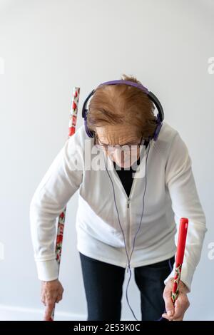 Fröhliche 90-jährige Frau genießen Musik in Kopfhörern, während Fegender Boden mit Besen und Hausarbeit Stockfoto