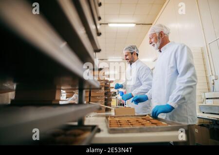 Arbeiter, die Kekse in Kisten packen, während sie in der Lebensmittelfabrik stehen. Stockfoto