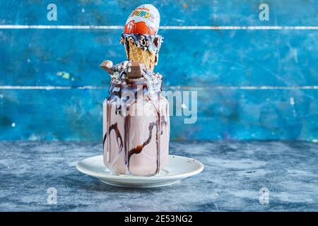Schokoladen-Smoothie mit Eiskegel, kinder Überraschung, Schokoladensirup auf dem weißen Teller im blauen Hintergrund Stockfoto