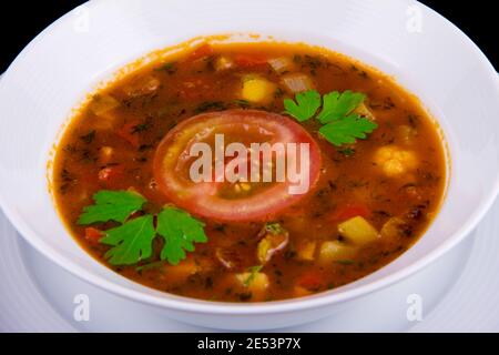 Ungarisches Gulasch - dicke Gemüsesuppe mit Rindfleisch und Tomaten auf weißem Boul auf schwarzem Hintergrund. Stockfoto