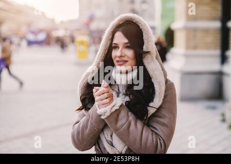 Nettes junges Mädchen im Wintermantel stehen in der Straße und wärmen ihre Hände. Stockfoto