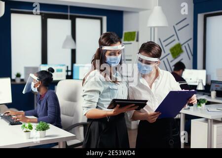 Geschäftsleute tragen Gesichtsmaske für covid19 Zusammenarbeit im Büro. Multiethnisches Geschäftsteam, das während der globalen Pandemie mit Coronavirus soziale Distanz respektiert. Stockfoto