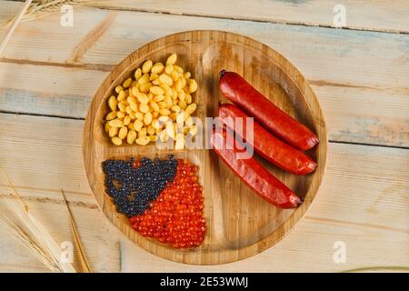 Würste, gekochte Maiskörner und Kaviar auf einem Holzteller Stockfoto