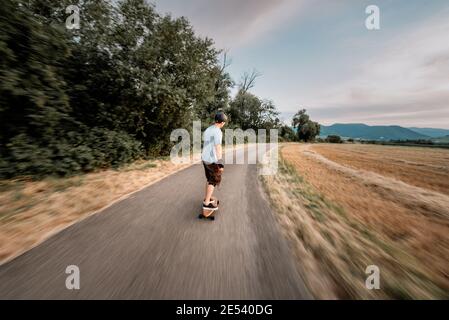 Der Mann reitet auf einem Longboard die Straße hinunter Stockfoto