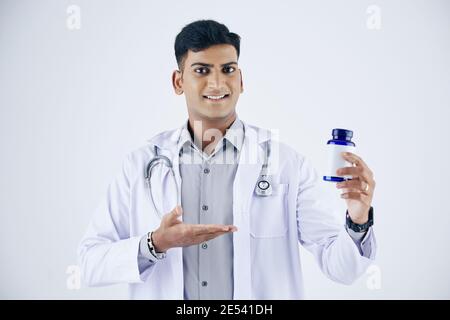 Porträt eines glücklichen schönen jungen indischen Hausarzt zeigt Plastikflasche mit Pillen und Tabletten, isoliert auf weiß Stockfoto