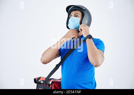 Develiry Mann in medizinische Maske mit Kühltasche auf seinem Schulter auf Helm setzen Stockfoto