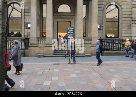 Buchanan Street, Glasgow, Schottland, Großbritannien. Ein Mann steht vor dem Apple-Einzelhandelsgeschäft mit einem Plakat, das billigere Apple-Reparaturen wirbt Stockfoto