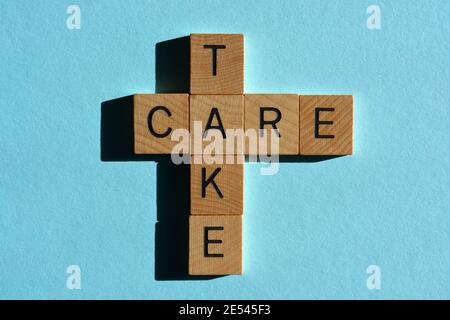 Take Care, Wörter in Holz-Alphabet Buchstaben in Kreuzworträtsel-Form isoliert auf blauem Hintergrund Stockfoto