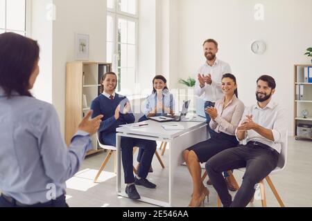 Geschäftsleute Kollegen sitzen im Büro und applaudieren stehende Frau Kollege nach erfolgreicher Präsentation Stockfoto