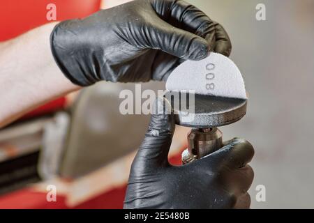 Handschellen, die Schleifpapier auf einen Polierer legen. Schleifscheiben. Polierwerkzeuge und Arbeitskonzept Stockfoto