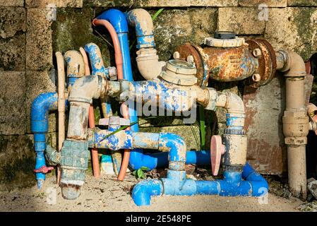 Verwirrende Details von rostigen Wasserzählern, Ventilen und blauen pvc-Rohren außerhalb einer schmutzigen Hauswand Stockfoto